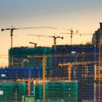 A cityscape featuring high-rise buildings under construction with cranes during sunset.