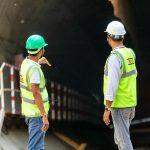 Two construction workers examine a tunnel entrance, highlighting safety and teamwork in infrastructure projects.