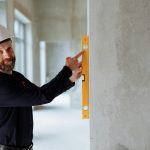 Confident engineer with hard hat using a spirit level on a wall at a construction site.