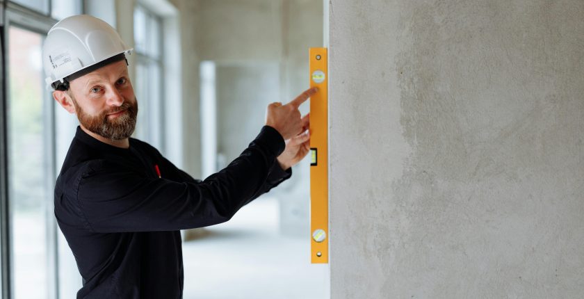 Confident engineer with hard hat using a spirit level on a wall at a construction site.