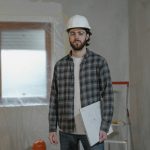 Adult male construction worker holding blueprints in an indoor renovation site.
