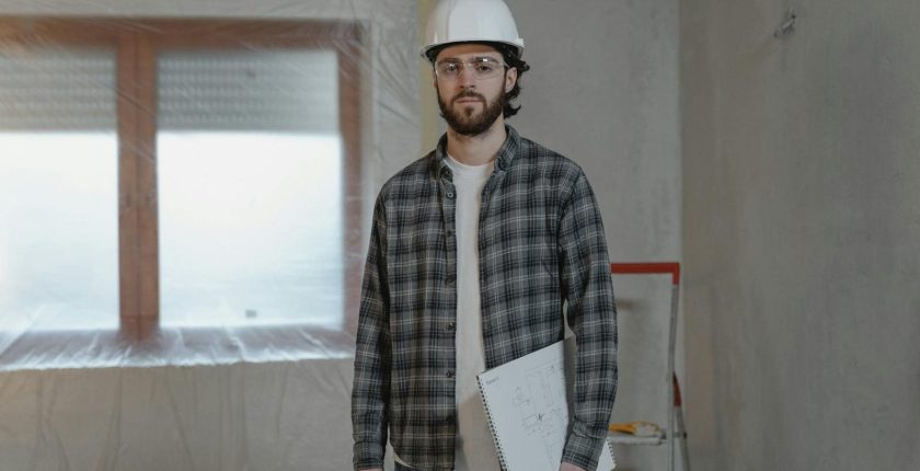 Adult male construction worker holding blueprints in an indoor renovation site.