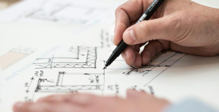 Close-up of hand drawing intricate technical designs on blueprint with pen, ideal for engineering or architecture themes.