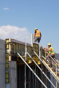 Two construction workers building a structure, embodying teamwork and safety under a clear blue sky.