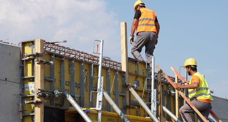Two construction workers building a structure, embodying teamwork and safety under a clear blue sky.