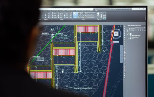 A civil engineer working on a weir design using CAD software on a computer screen in an office setting.