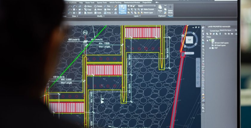 A civil engineer working on a weir design using CAD software on a computer screen in an office setting.