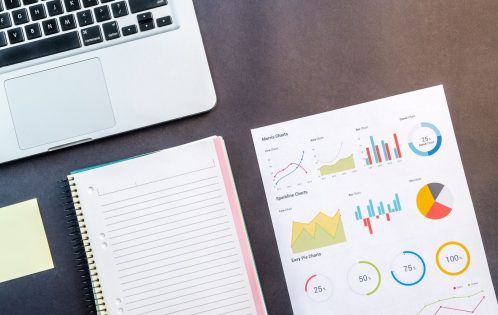 Top view of a laptop, notebook, and data charts on a table, ideal for business and work themes.