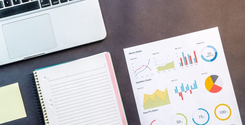 Top view of a laptop, notebook, and data charts on a table, ideal for business and work themes.
