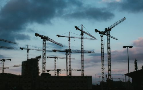 Multiple construction cranes silhouetted against the evening sky, capturing industrial progress.